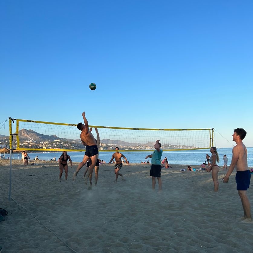 People playing beach volleyball in Spain at sunset, representing the active sports community supported by Flakex.