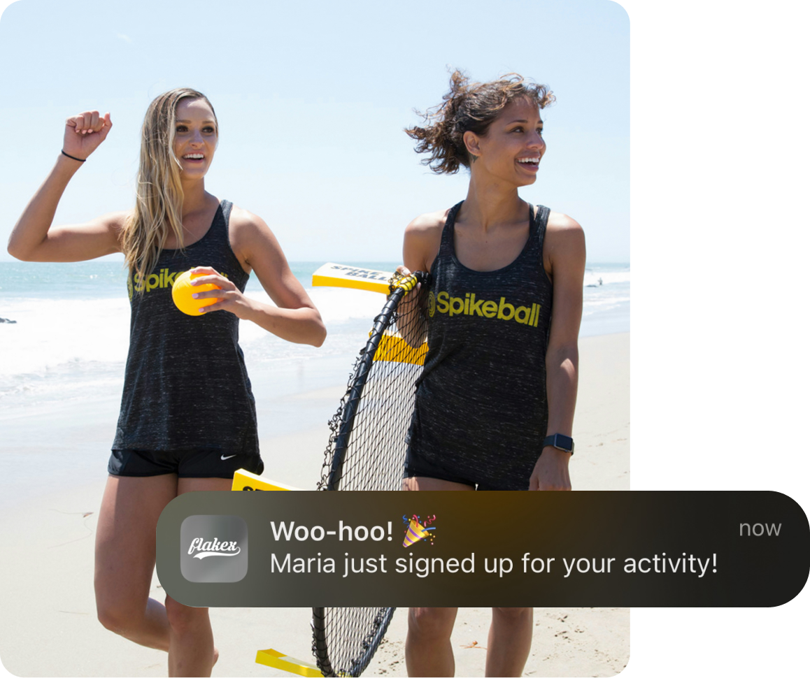 two girls on the beach walking and smiling. One of them holds a spikeball net to play. They added this sport activity on the Flakex app to invite more people to spikeball in Spain